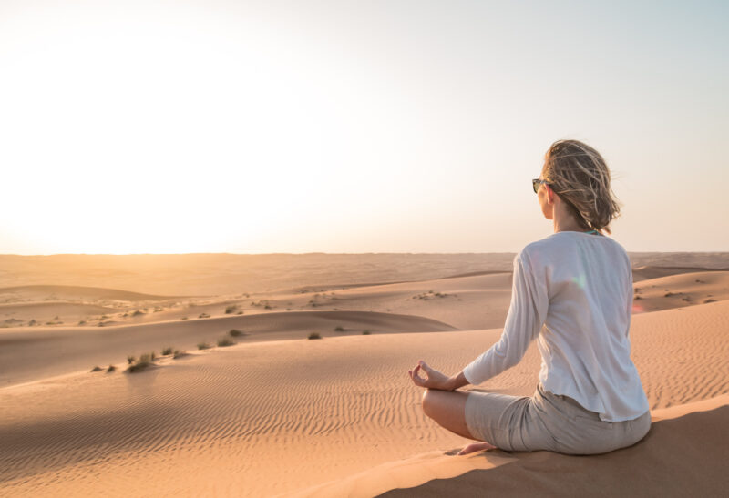 rear-view-of-woman-doing-yoga-at-desert-against-sky